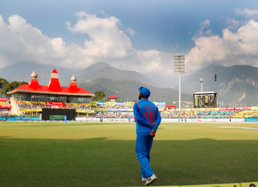 Aerial view of Dharamsala Cricket Ground with the snow-capped Dhauladhar mountain range in the background, showcasing the stadium's unique location.